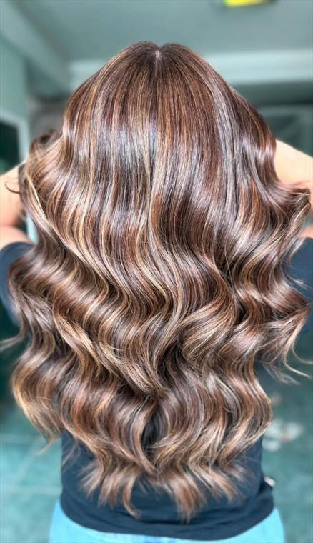 Rich brunette hair with warm caramel and honey balayage highlights in glossy waves