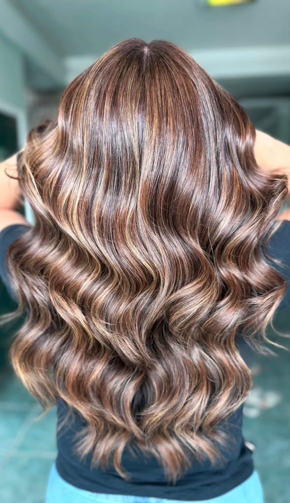 Rich brunette hair with warm caramel and honey balayage highlights in glossy waves